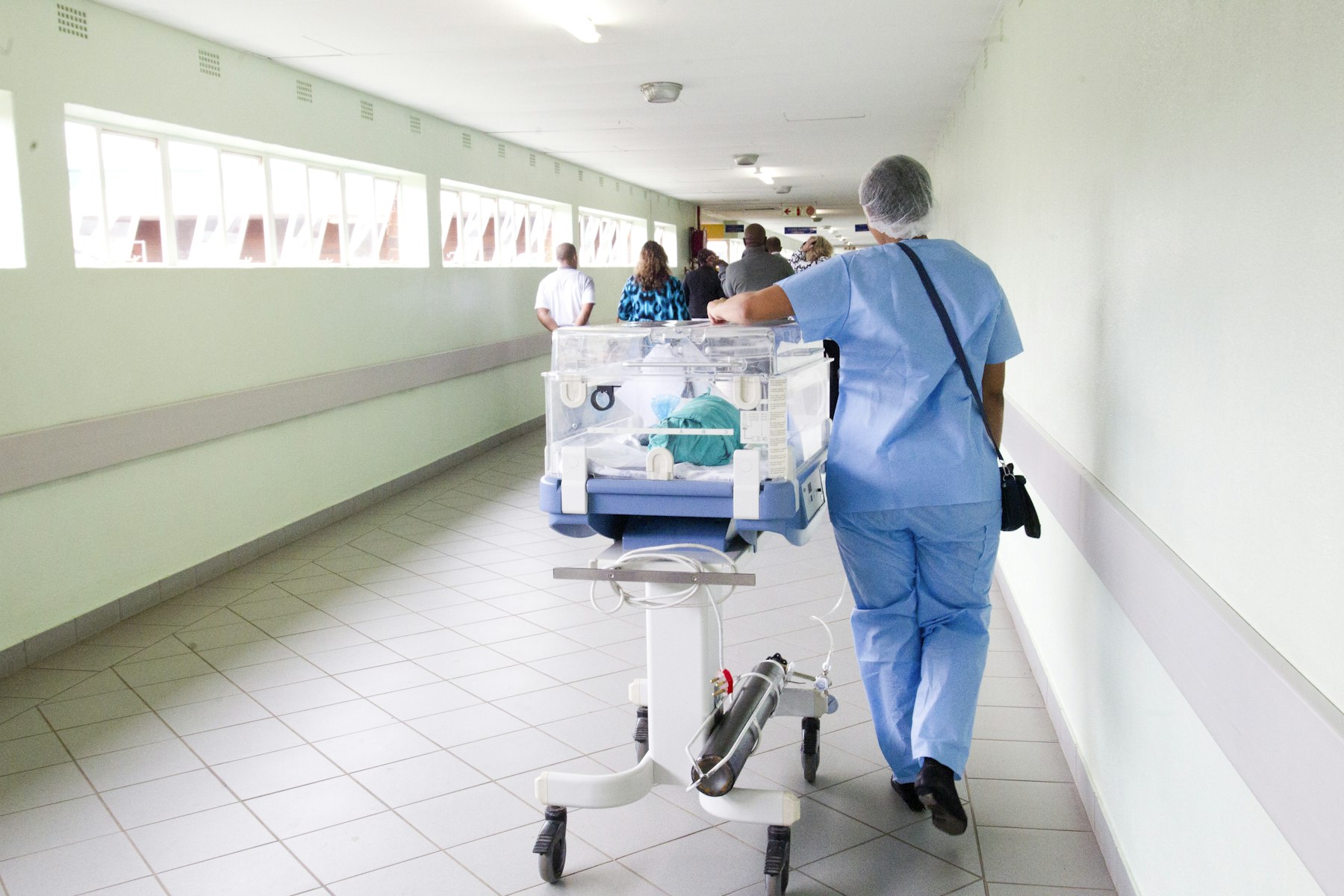Pflegekraft schiebt einen Inkubator durch einen Klinikflur